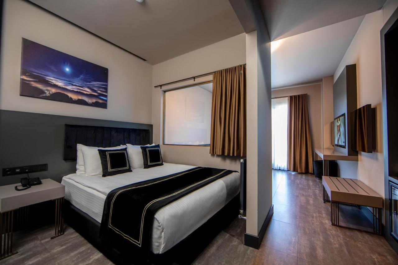 Menalo Hotel Premium Istanbul Airport Exterior photo The photo shows a modern hotel room featuring a neatly made bed with white linens and a black decorative runner. There are two pillows with black accents on the bed. The walls are painted in neutral colors, and there is a large window with curtains t