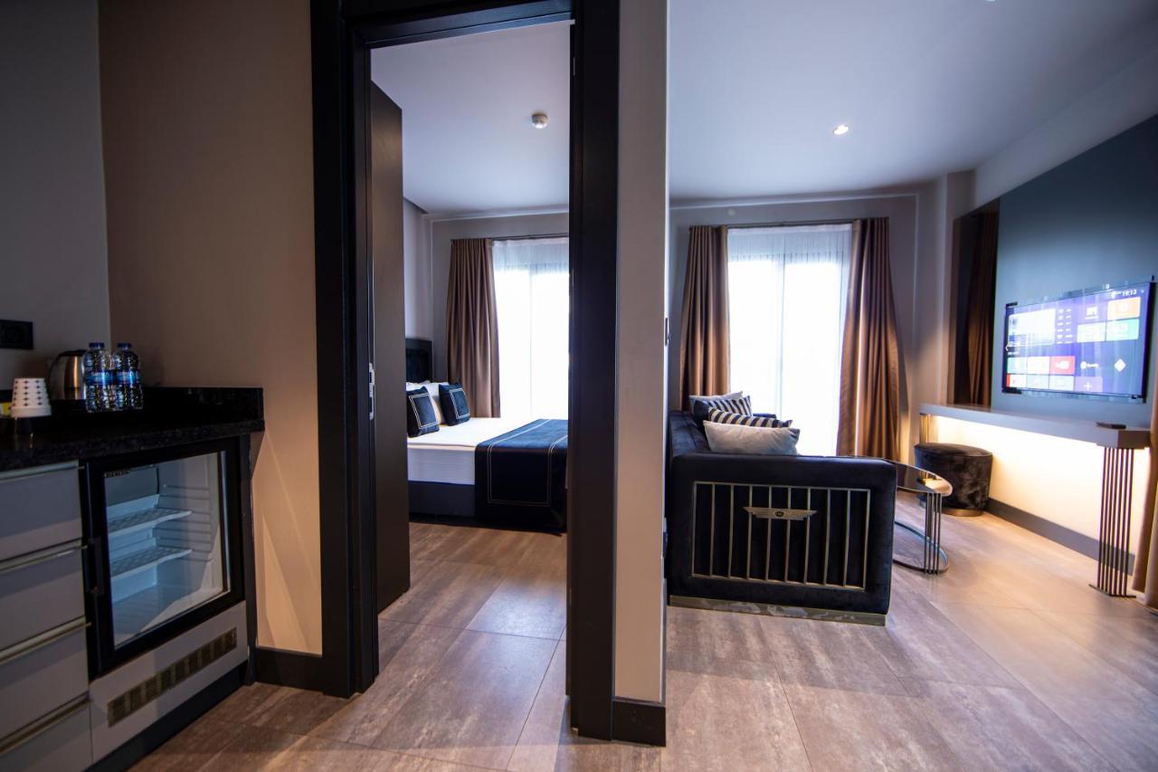 Menalo Hotel Premium Istanbul Airport Exterior photo The photo shows a modern hotel room or suite. In the foreground, there is a small kitchenette area with what appears to be a mini-fridge. Beyond the kitchenette, there is an opening leading into a bedroom area that features a large window with light-